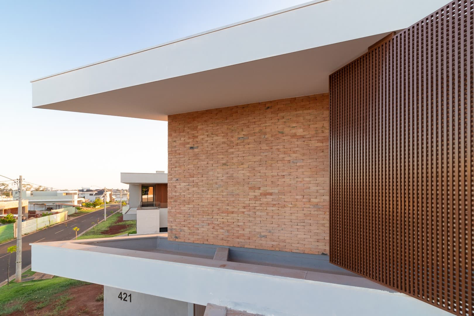 Casa CaCle – fachada com revestimento de tijolinho e ripas de madeira no contexto urbano