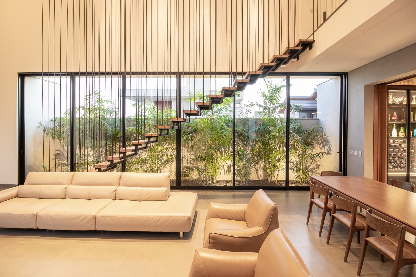 Casa CaCle – sala de estar com sofá, escada metálica e jardim de palmeiras ao fundo
