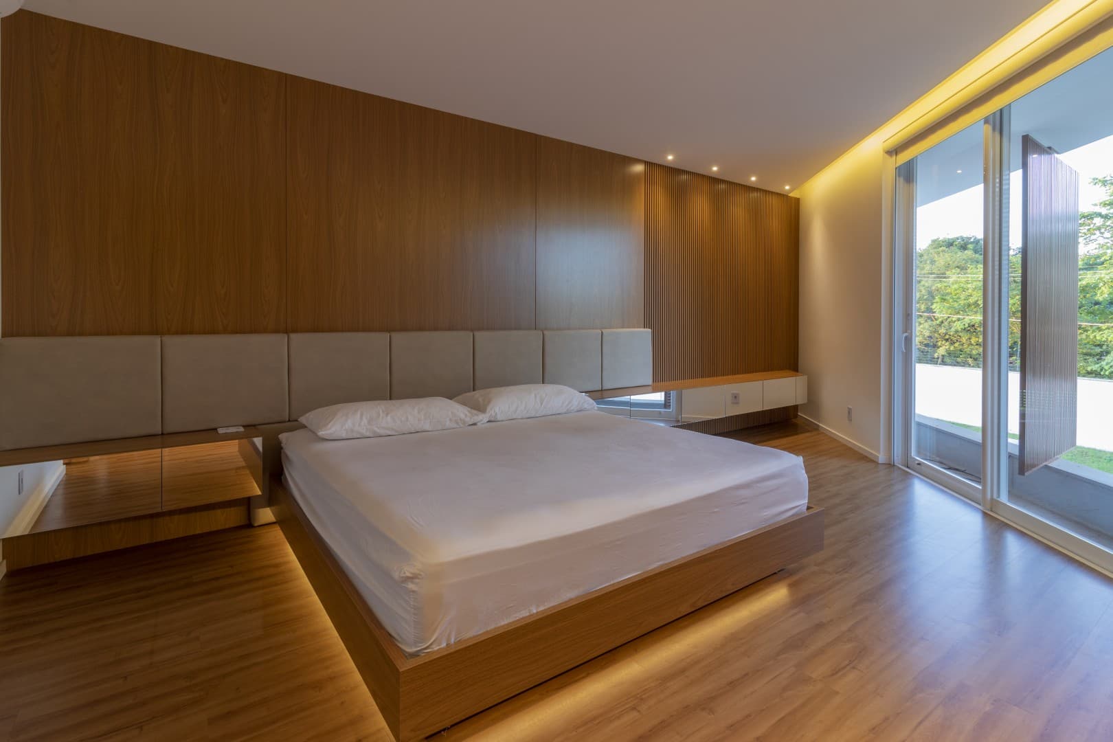 Casa CaCle – suíte master com cama, cabeceira em madeira e janelas para o jardim