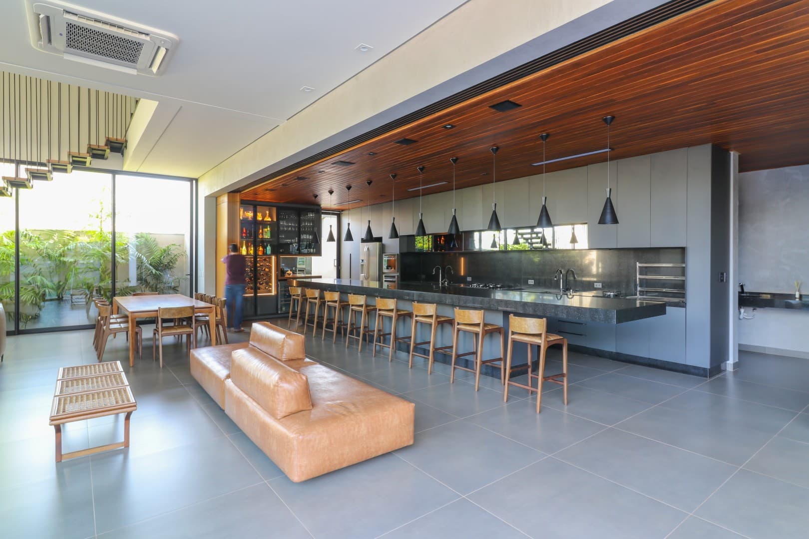 Casa CaCle – área gourmet com bancada em concreto, pendentes pretos e jardim externo