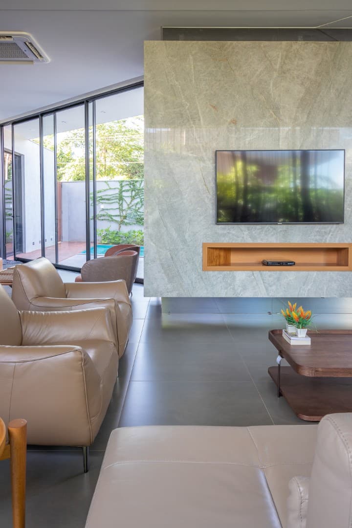 Casa CaCle – sala de estar com poltrona em couro, rack em madeira e vista para piscina