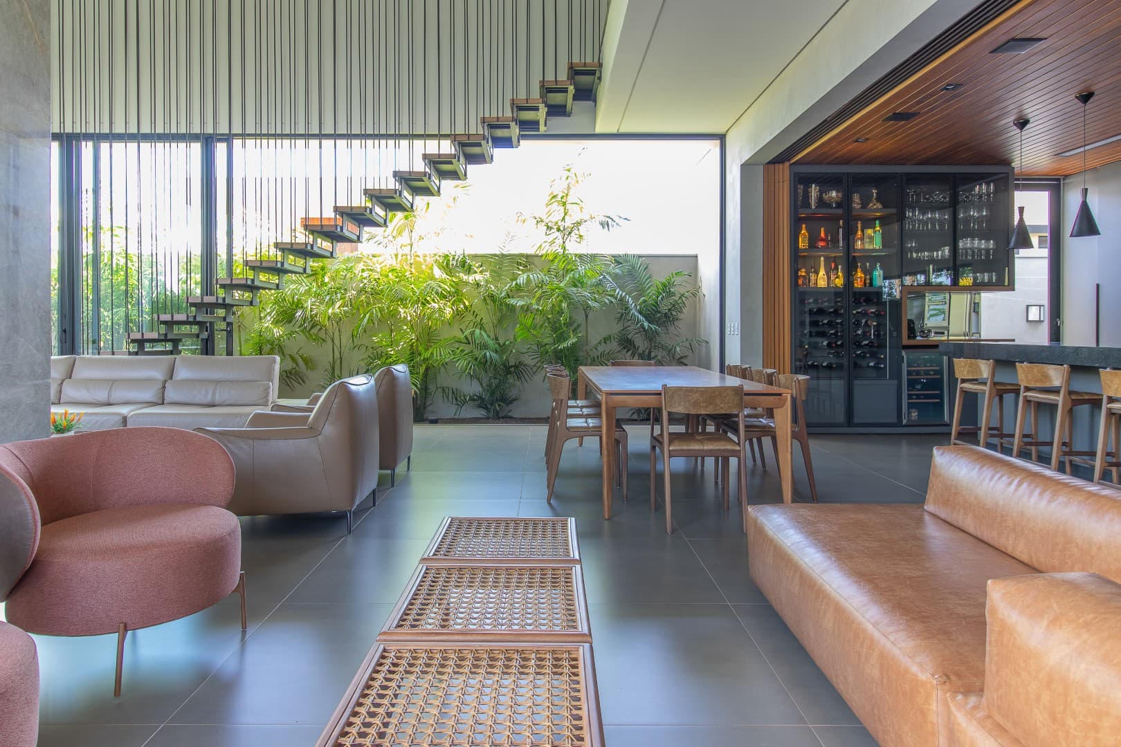 Casa CaCle – área de lazer com sofás, mesa de jantar, jardim vertical e adega ao fundo