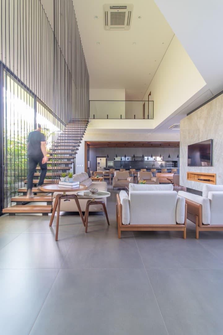 Casa CaCle – sala de estar com sofás, lareira, TV e escada com cobogós ao fundo