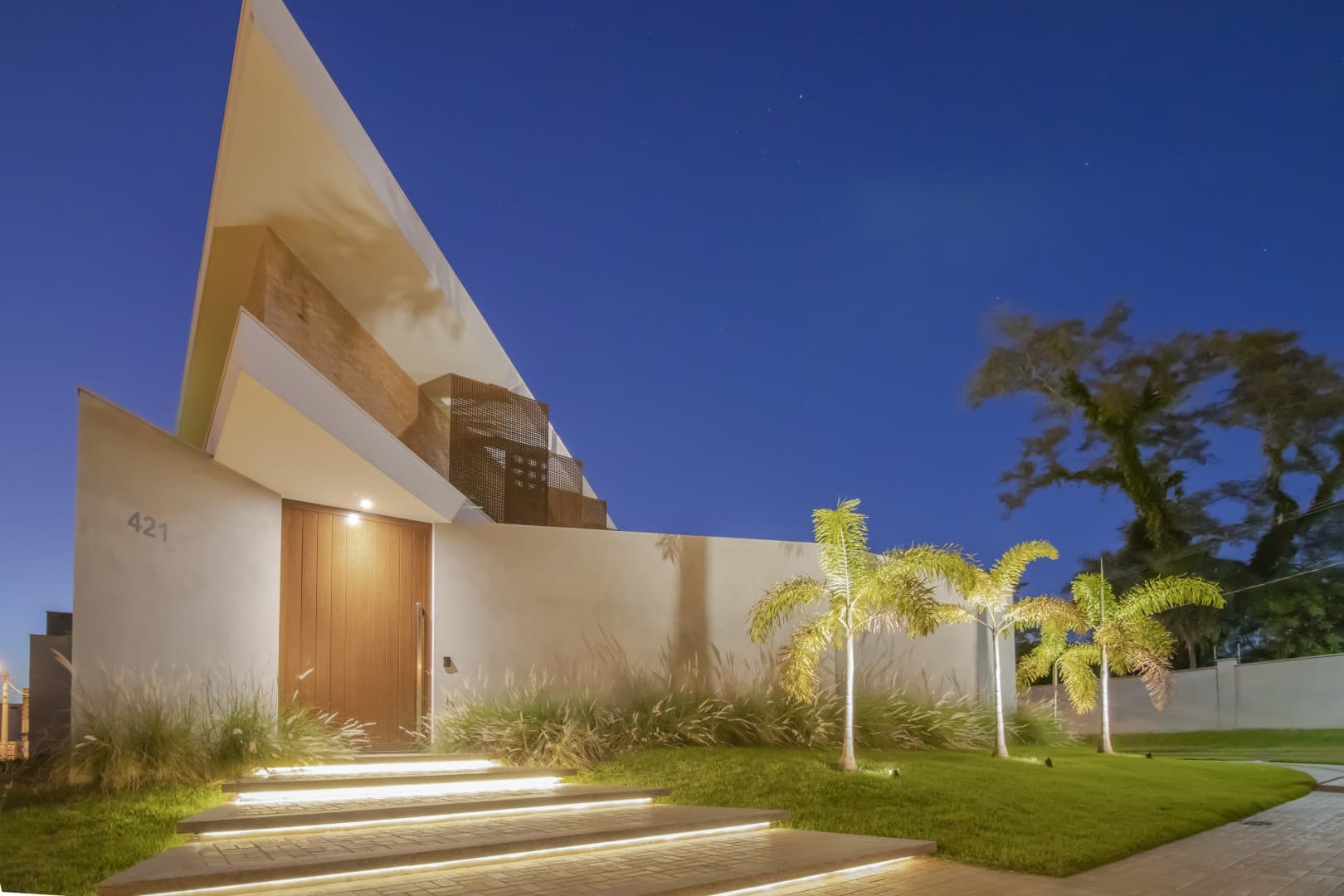 Casa CaCle – fachada noturna com entrada iluminada, número 421 e árvore ao fundo